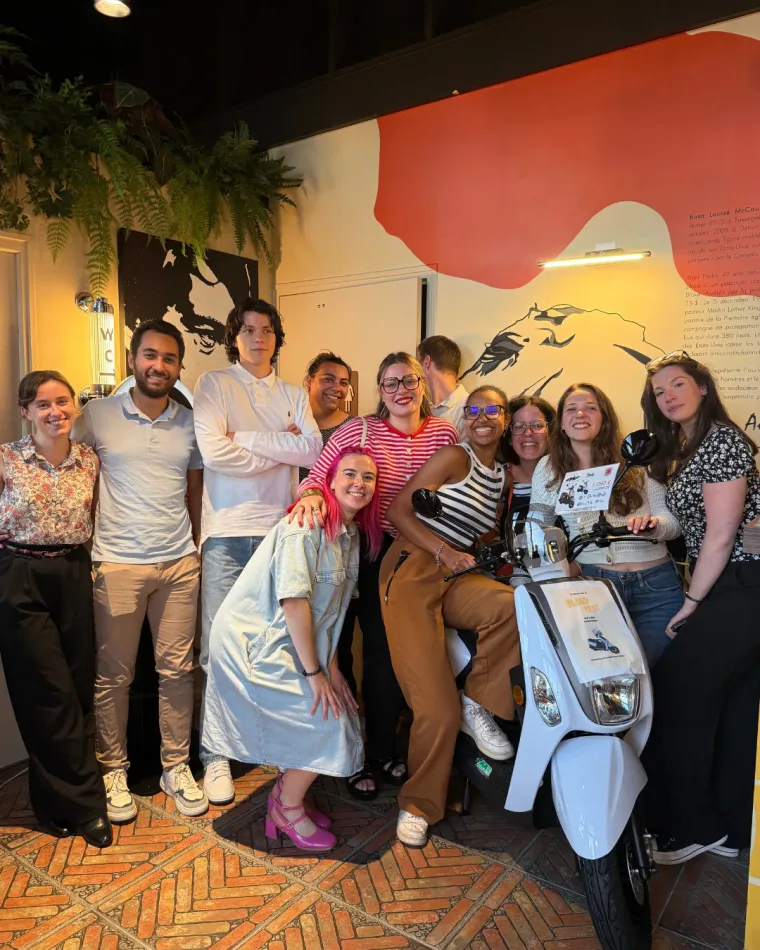 Un groupe pose dans la salle autour du scooter du blind test, devant la fresque murale