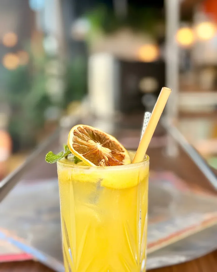 Un cocktail jaune à la rondelle d'orange séchée et à la menthe, posé sur le comptoir