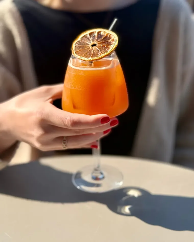 Un cocktail orange en verre à pied, décoré d'une rondelle d'orange séchée, tenu au soleil