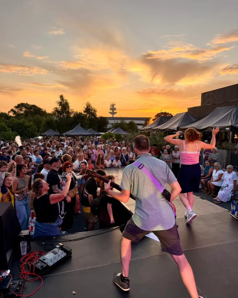 Un groupe en concert sur la scène en plein air, devant la foule, au coucher du soleil