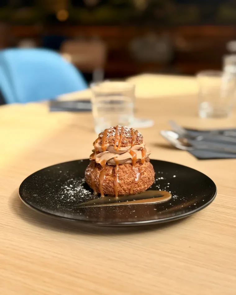 Un chou garni, nappé de caramel et saupoudré de sucre glace, sur une assiette noire