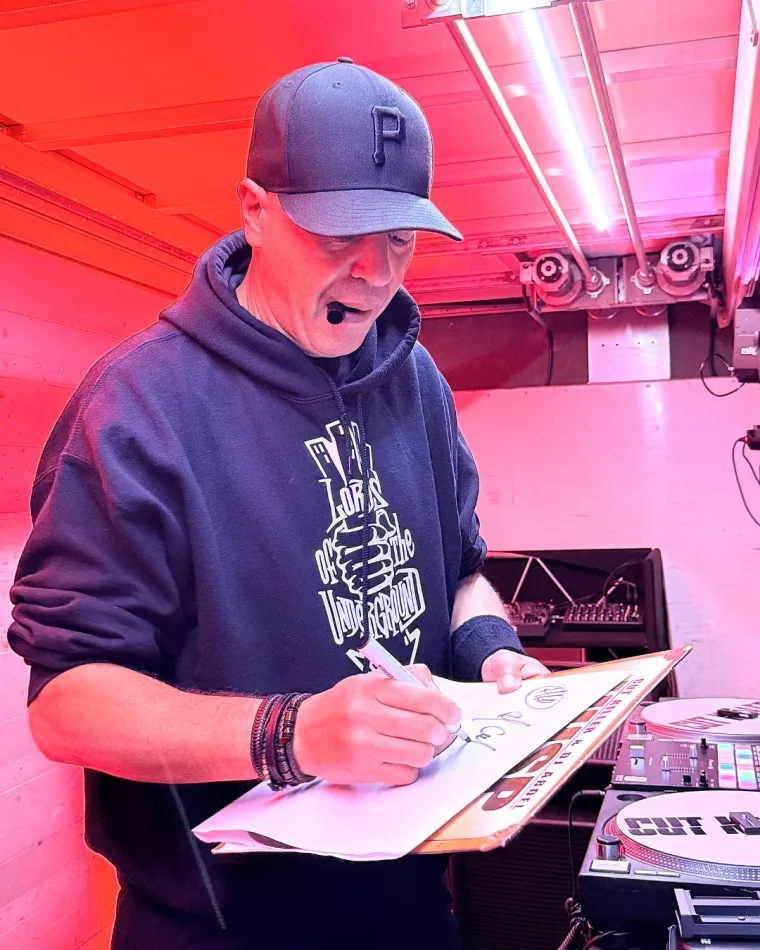 Dédicace d'une pochette de vinyle derrière les platines, sous les lumières roses