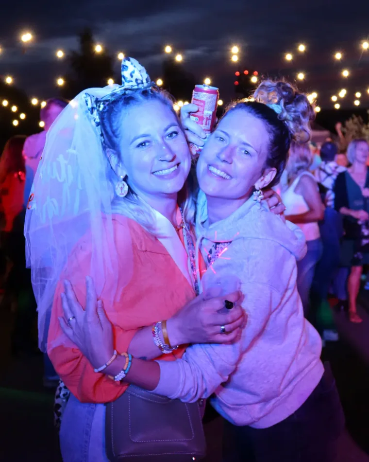 Une future mariée en voile et une amie enlacées, pendant une soirée sous les guirlandes