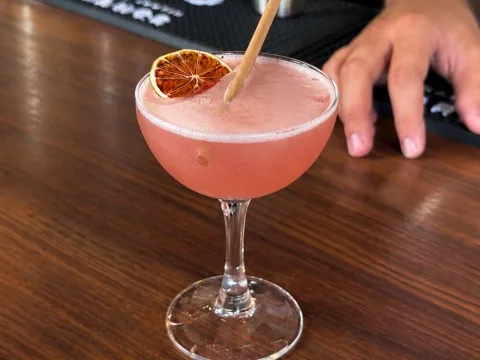 Cosmopolitan rose servi en coupe avec un citron séché, posé sur un comptoir en bois