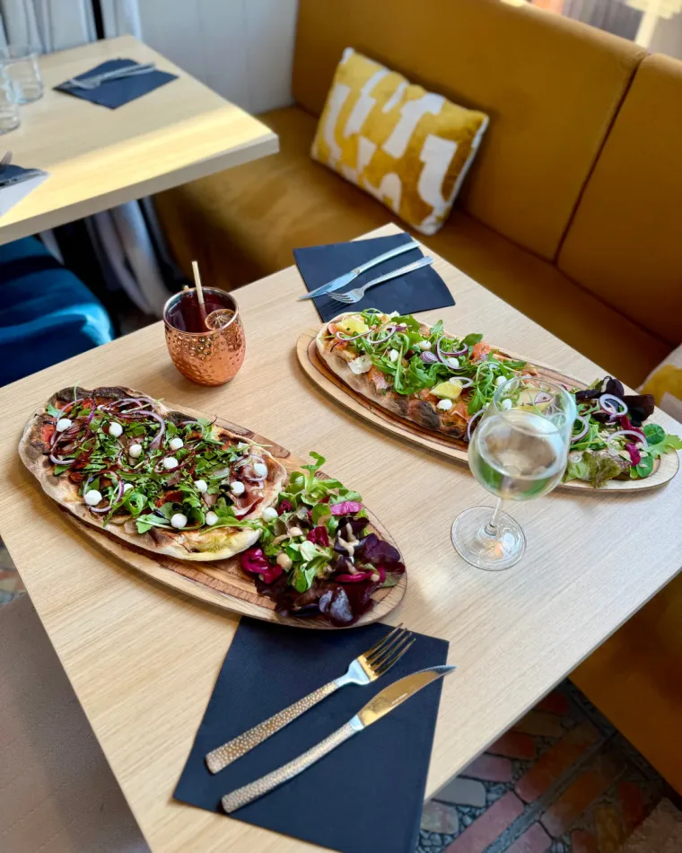 Deux pinsas garnies de roquette servies sur planche, avec un cocktail en tasse cuivrée