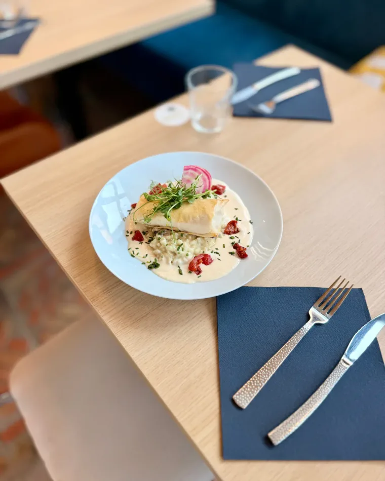 Un filet de poisson croustillant sur un risotto à la sauce crémeuse, avec tomates et jeunes pousses