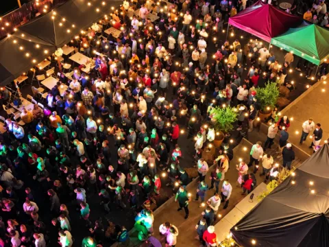Vue plongeante sur une grande soirée en plein air, entre les tentes et sous les guirlandes lumineuses
