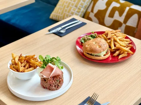 Un tartare de bœuf et un burger servis avec leurs frites, sur une table de la salle