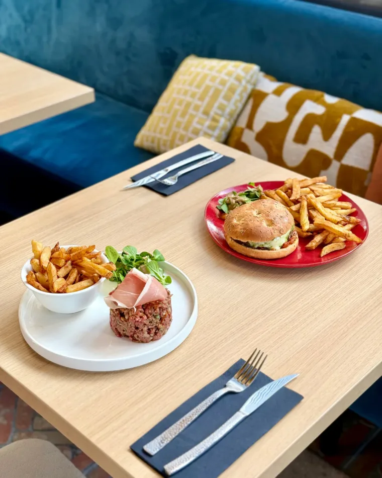 Un tartare de bœuf et un burger servis avec leurs frites, sur une table de la salle
